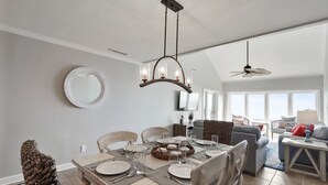 A dining area with a table set for four, a ceiling fan, and a large window offering a view of the outdoors.