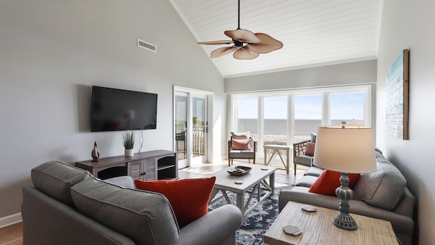 A living room with a large TV, grey sofas, a coffee table, and a ceiling fan.