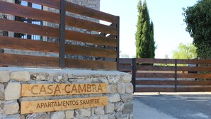 Un mur de pierre sur lequel sont fixées des panneaux en bois indiquant « CASA CAMBRA » et « APARTAMENTOS SAMITIER ».