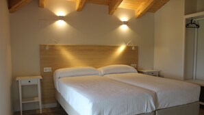 Un lit double avec une tête de lit en bois, deux tables de chevet et deux lampes fixées au mur.