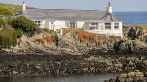 Un bâtiment situé sur la côte, doté d’une façade en pierre, de grandes fenêtres et d’une cheminée imposante.