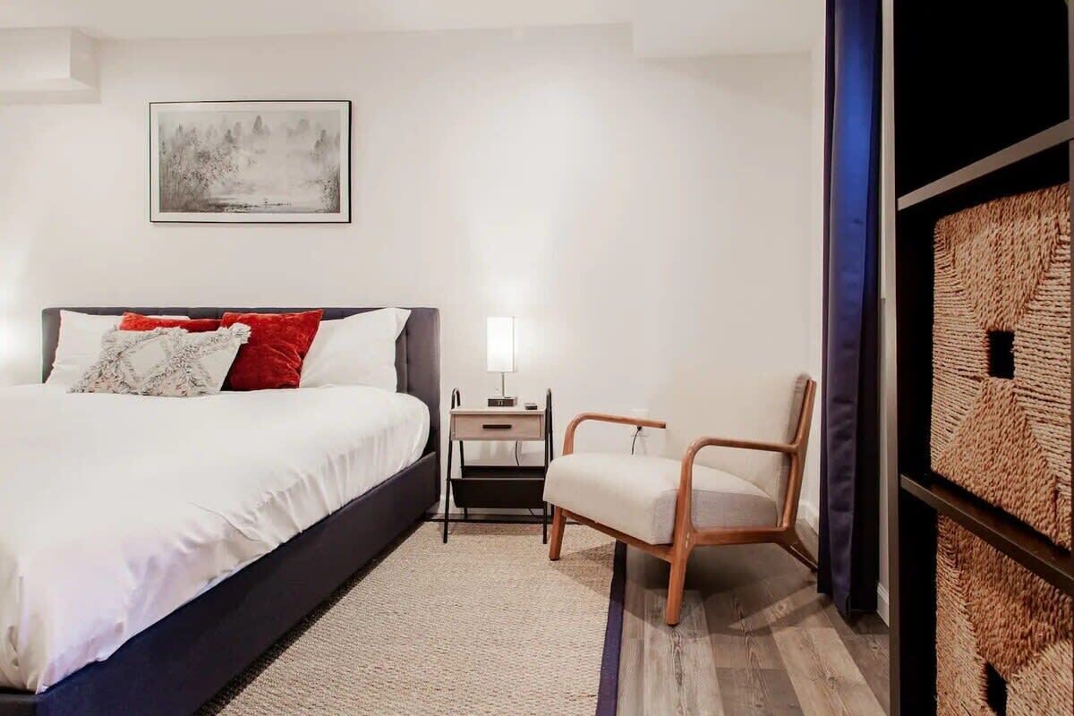 Une chambre moderne avec un grand lit, une table de chevet, une chaise et une œuvre d’art accrochée au mur.