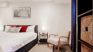 Ein modernes Schlafzimmer mit einem großen Bett, einem Nachttisch, einem Sessel und einem Wandbild.