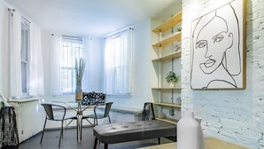 A modern living room with a dining area, featuring a white brick wall, a large window, and a minimalist art piece. - Dupont Circle sub station DC Apart High speed WiFi (Washington)