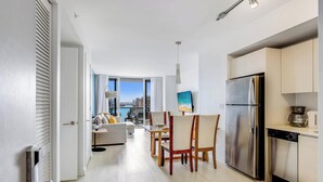 A modern kitchen with a stainless steel refrigerator, a dining area with a table and chairs, and a living room with a sofa and a view of the city. - 2BR Apartment w/ Balcony - Near Beach (Hallandale Beach)