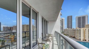 A balcony with large windows, a pool, and a cityscape view.