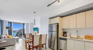 A modern apartment with a dining area, kitchen, and a large window overlooking a cityscape.