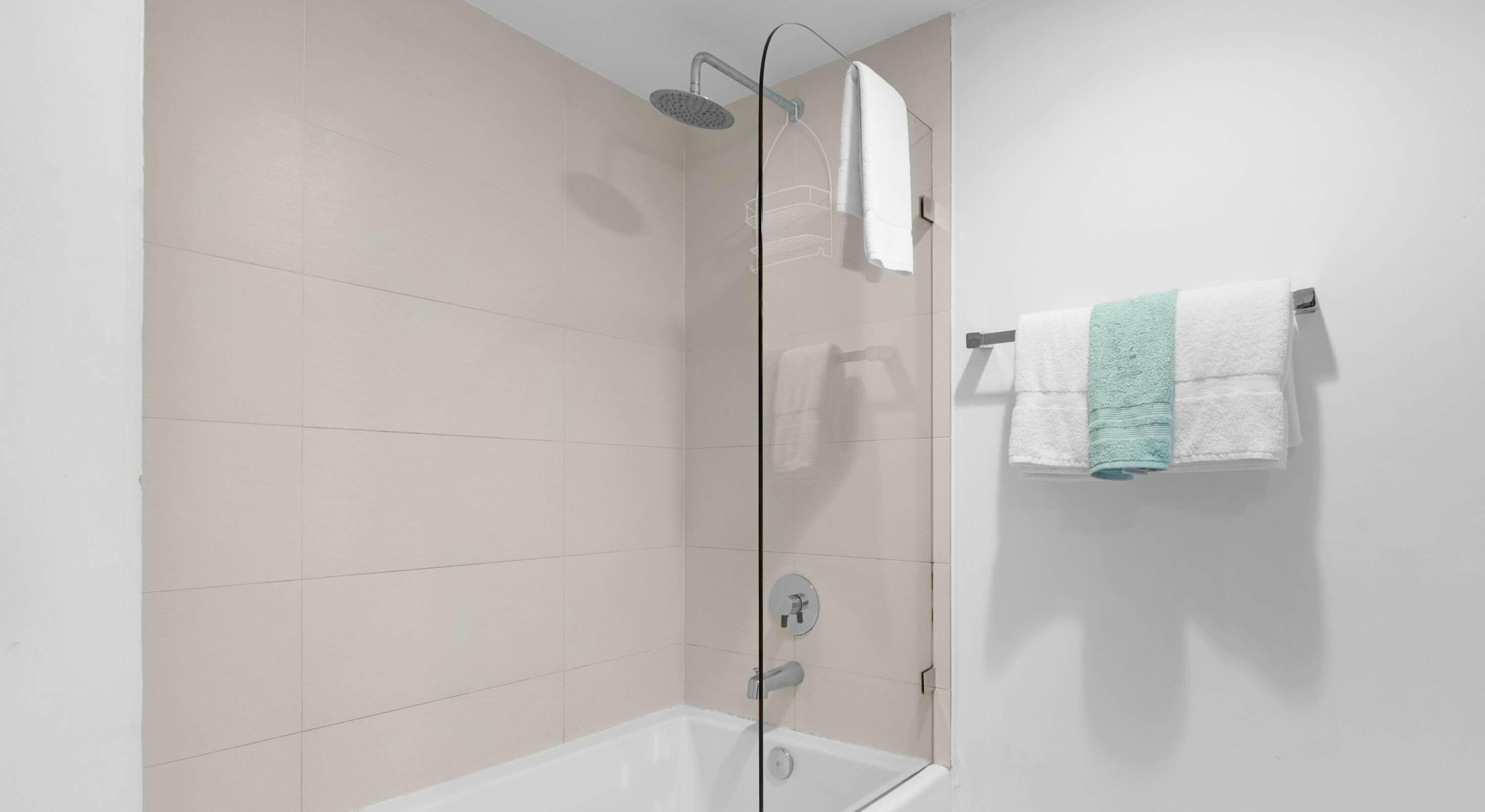 Een moderne badkamer met een douchecabine van glas, een wit bad en een handdoekrek met twee handdoeken.