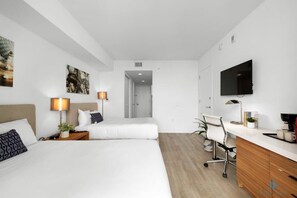 A modern hotel room with two beds, a desk, a TV, and artwork on the walls.
