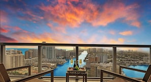 A balcony with a city view, a table with bottles and grapes, and a chair.