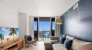 A modern living room with a television, a sofa, a chair, and a balcony with a view of the city and water.