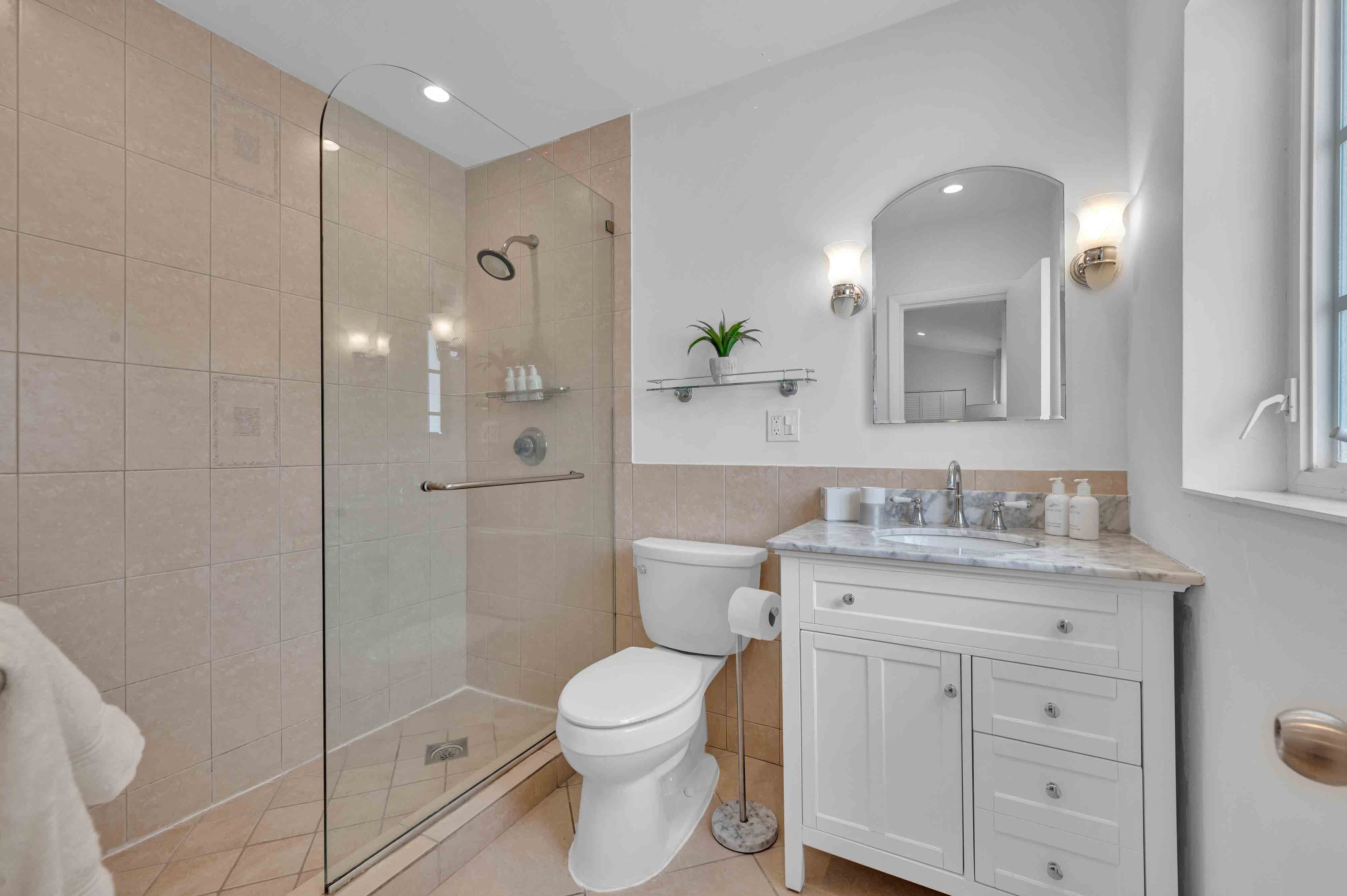 A modern bathroom with a glass-enclosed shower, a toilet, a sink with a marble countertop, and a mirror above the sink.