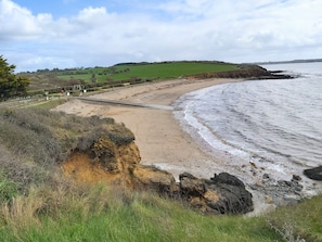 Un paysage côtier avec une plage de sable, une côte rocheuse et une colline herbeuse en arrière-plan.