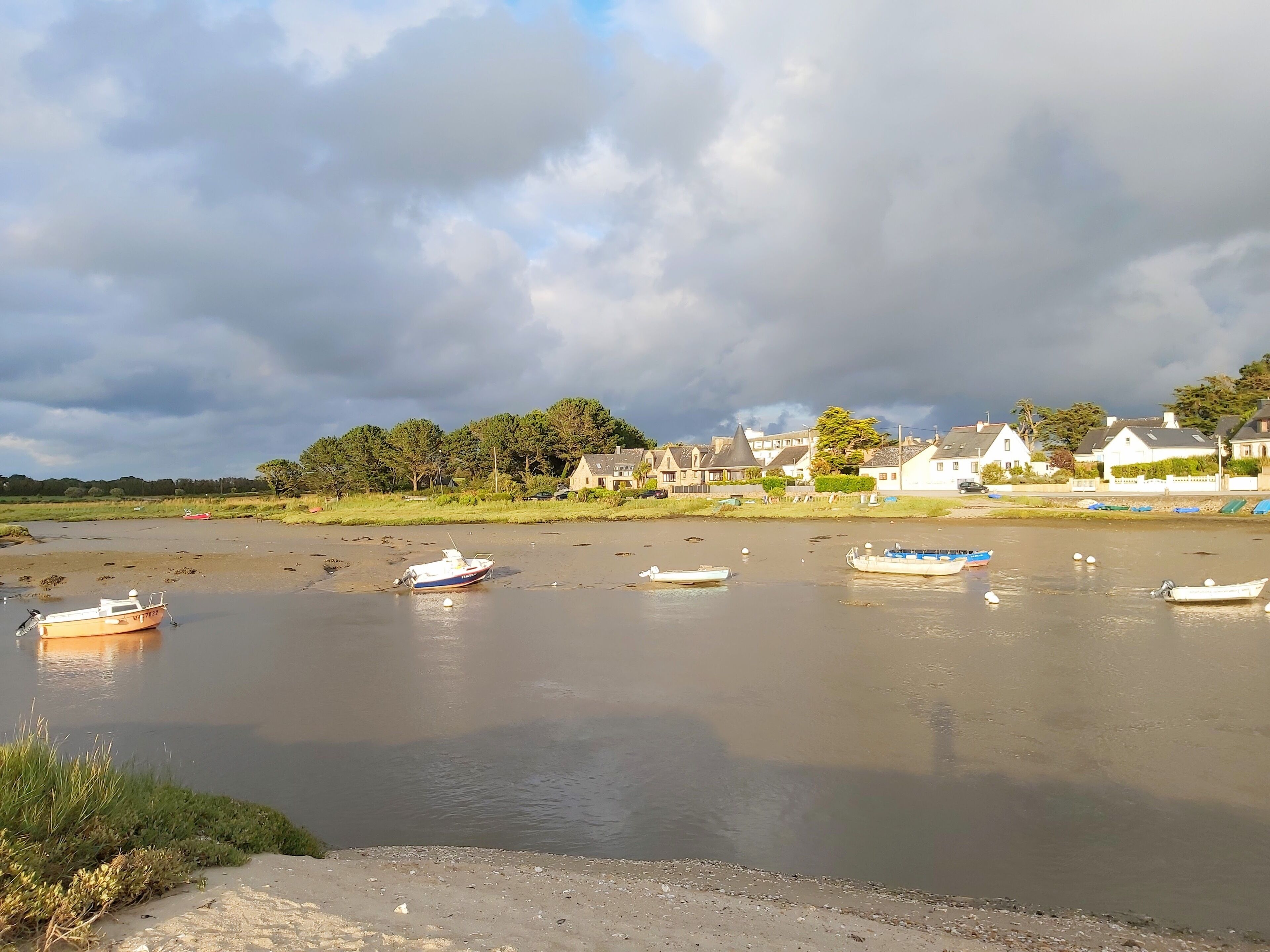 A riverside view with boats, houses, and a cloudy sky.
