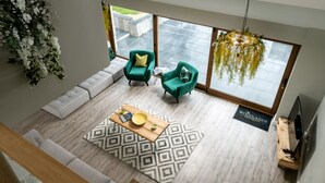 Een ruime woonkamer met een groot raam, een zithoek, een houten salontafel en een hanglamp.