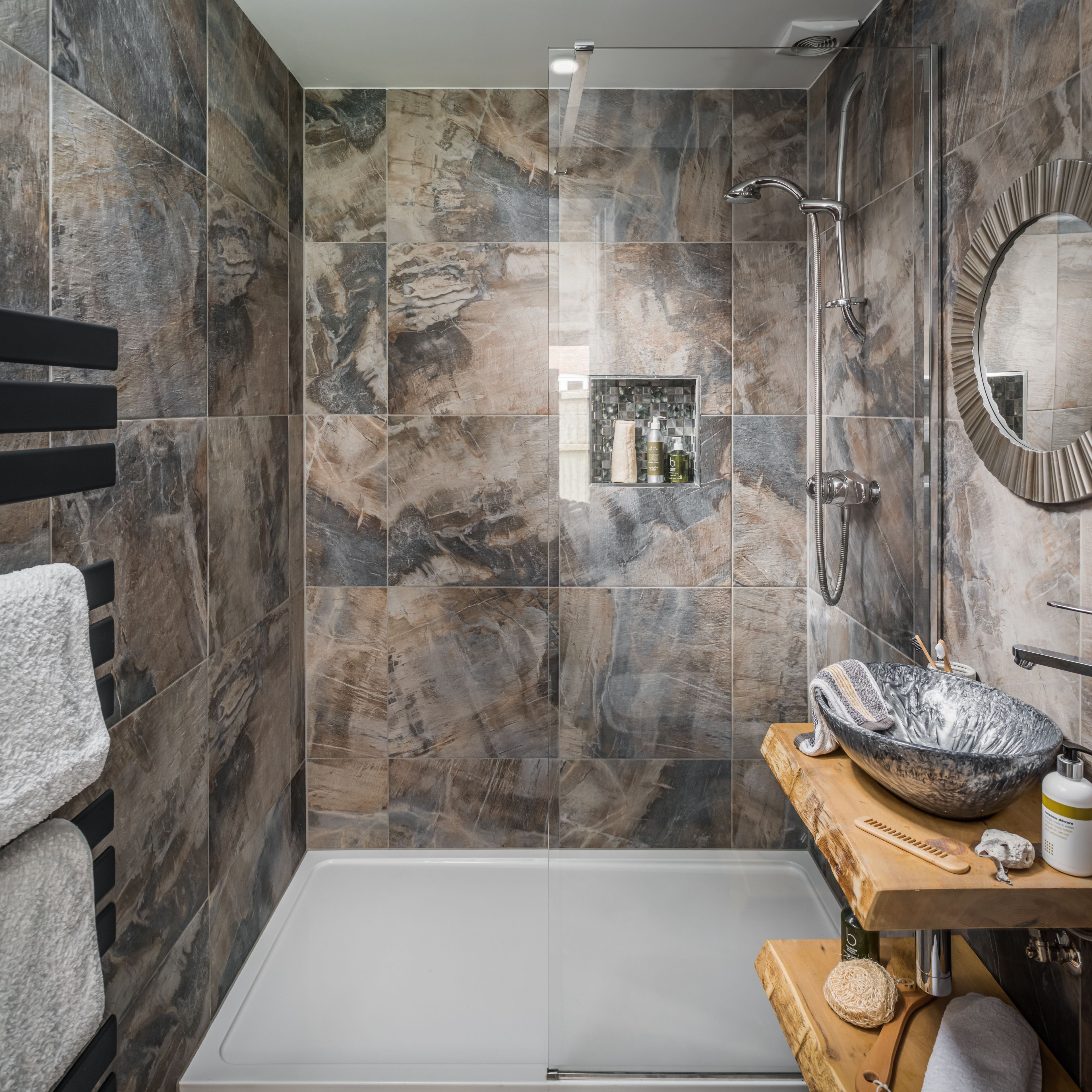 Een moderne badkamer met een douchecabine van glas, een betegelde wand van marmer, een houten wastafelmeubel met een grote waskom en een handdoekhouder.