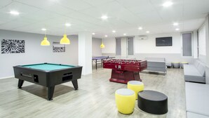 Un salón recreativo moderno con mesa de billar, mesa de futbolín y zona de estar.