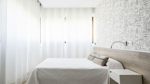 Un dormitorio con cama, mesita de noche, pared decorada y ventana con cortinas.