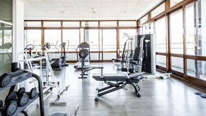 Un gimnasio con diversos equipos de ejercicio, amplias ventanas y un diseño limpio y moderno.