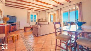 A living room with a sofa, TV, and dining table. - Villa AZALEA by Abahana Villas (Teulada)