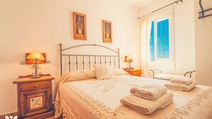 A bedroom with a bed, two bedside lamps, a nightstand, a window with curtains, and two framed pictures on the wall. - Villa AZALEA by Abahana Villas (Teulada)