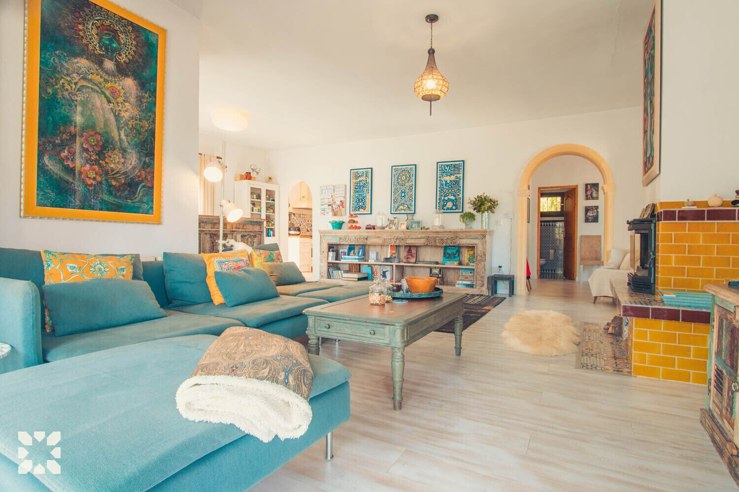 A spacious living room with a large sofa, a coffee table, and a fireplace. There are decorative tiles on the walls and a large painting above the sofa.