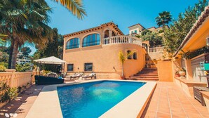 Zona de piscina con pileta, sillas de descanso y una escalera que lleva a un edificio con grandes ventanales y un balcón.