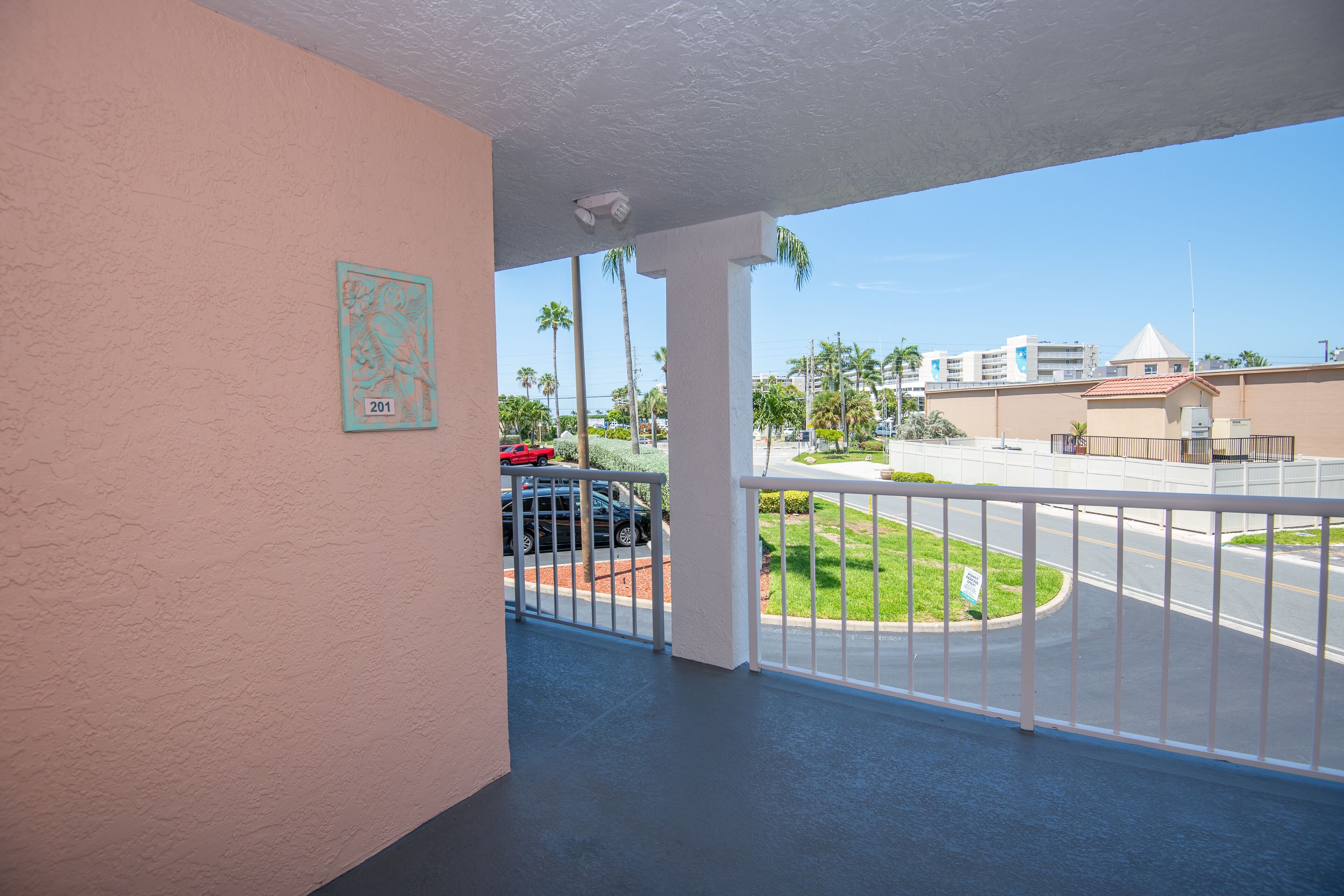 A balcony with a view of a street, a security camera, and a number plaque on the wall.