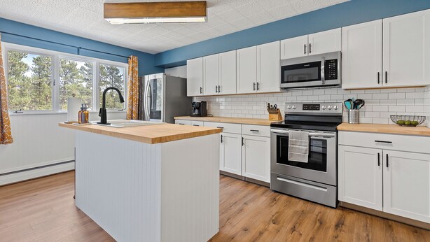 A modern kitchen with white cabinets, a central island, stainless steel appliances, and a view of the outdoors. - Blue Roof Lodge: Pet-Friendly, Walkable to Downtown Custer (Custer)