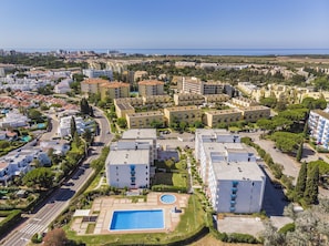 A residential area with multiple apartment buildings, a swimming pool, and a road. - Pé do Lago 1 Bedroom Apartment with Pool (Loulé)