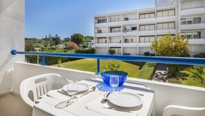Ein Balkon mit Esstisch, der auf ein Gebäude und einen gepflegten Garten blickt.