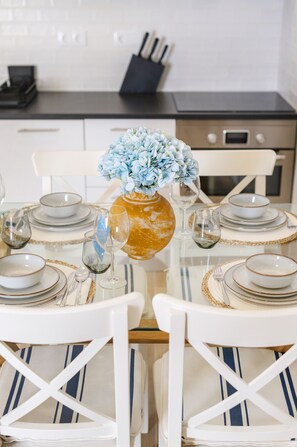 Une table à manger dressée avec des assiettes, des bols et des couverts, agrémentée d’un vase de fleurs et d’un verre de vin.