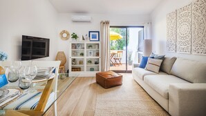 A modern living room with a sofa, a glass dining table with plates and glasses, a cabinet with decorative items, and a sliding glass door leading to an outdoor area. - BnBird Sunny Algarve @ Vilamoura (Loulé)