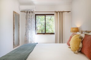 Quarto com cama, janela com cortinas, ar condicionado fixado na parede e luminária.