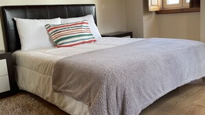 Un dormitorio con una cama, una mesita de noche, un ventanal y suelo de madera.