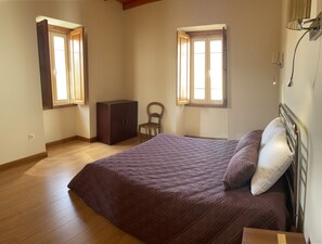 A bedroom with a bed, a wooden wardrobe, and two windows.