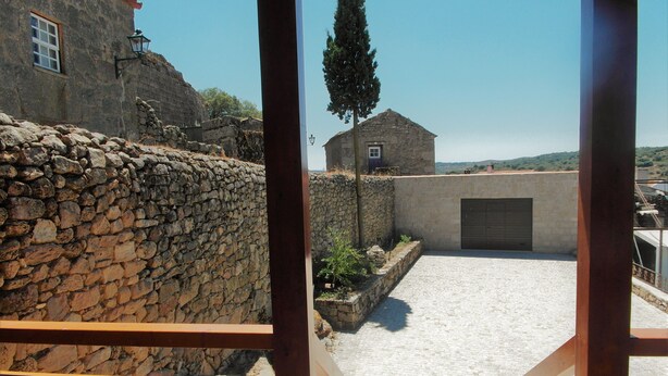 Un muro de piedra, un edificio con una puerta y un cielo despejado.