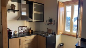 Cocina compacta con armarios de madera, encimera negra, pileta de acero inoxidable y ventana con vistas a las montañas.