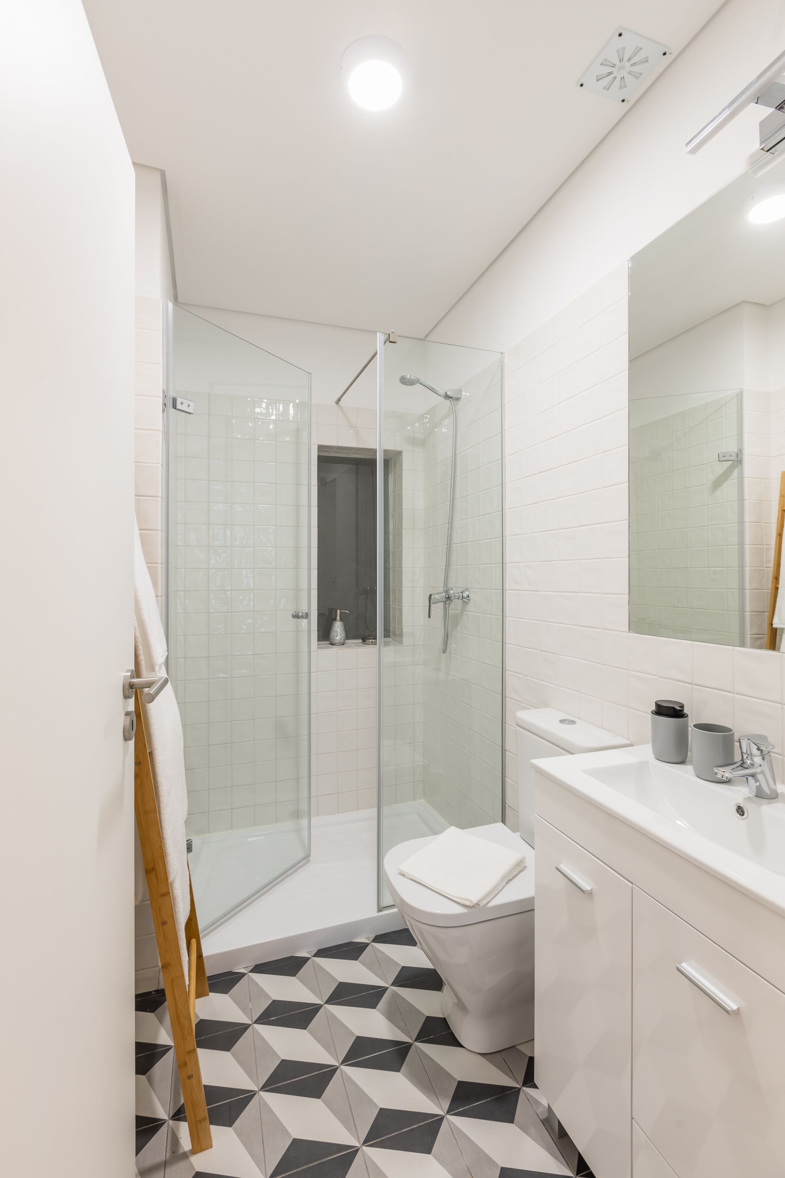 A modern bathroom with a glass shower enclosure, a white sink, and a tiled floor.
