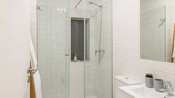 A modern bathroom with a glass shower enclosure, a white sink, and a tiled floor.