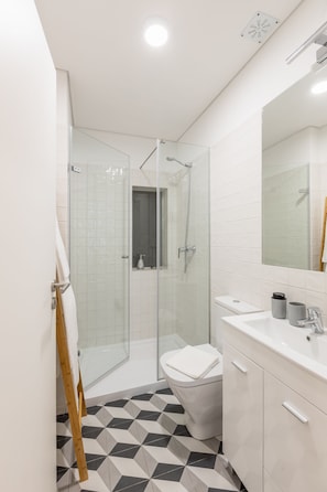 Un baño moderno con cabina de ducha de vidrio, un lavabo blanco y suelo de baldosas.