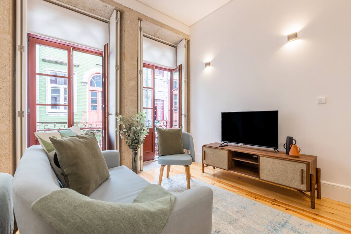 Un salon moderne avec un canapé, un téléviseur posé sur une console en bois et de grandes fenêtres dotées de portes rouges.