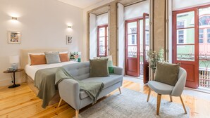 Quarto moderno com uma cama grande, um sofá cinzento e piso de madeira.