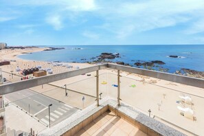 A beach view from a balcony with a clear sky, a sandy beach, and rocky outcrops.