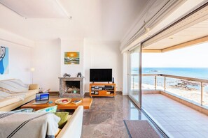 A spacious living room with a fireplace, a television, and a balcony with a view of the beach.
