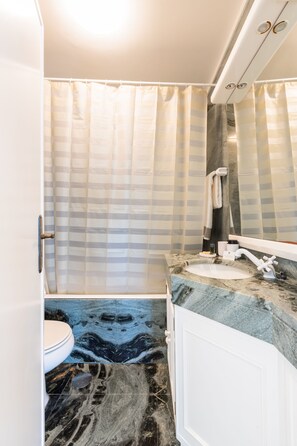 A bathroom with a striped shower curtain, a marble sink, and a white toilet.