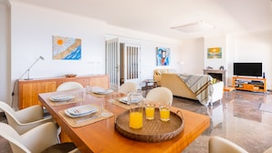 A modern hotel room with a dining area, a sofa, a TV, and artwork on the walls. - Povoa Sunset Views (Povoa De Varzim)