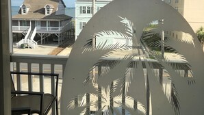 Une vue d’une maison de plage dotée d’un balcon, d’un escalier menant au porche et, au premier plan, de la silhouette d’un palmier.
