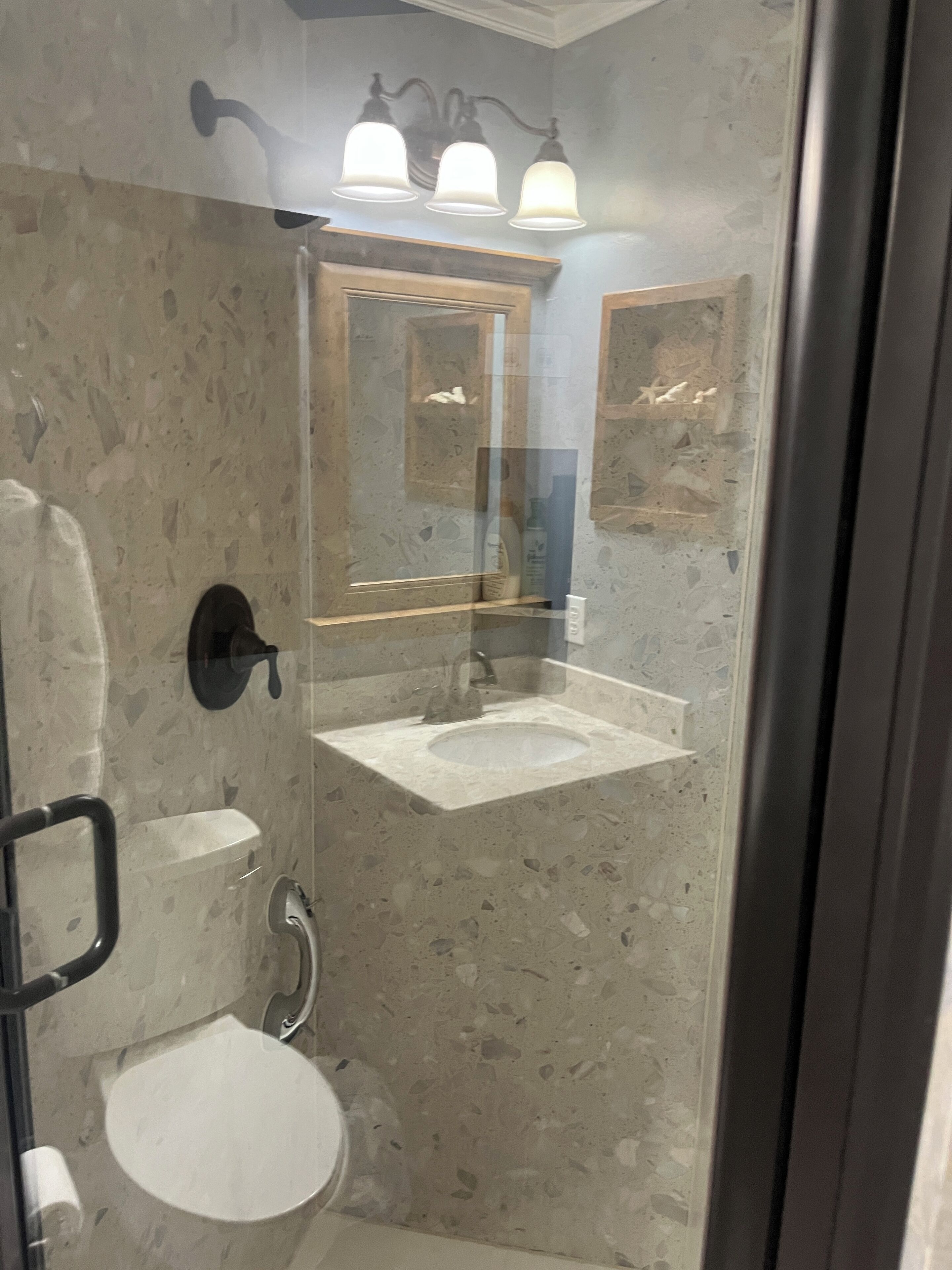 Een badkamer met een douchecabine van glas, een witte wastafel en een spiegel boven de wastafel.
