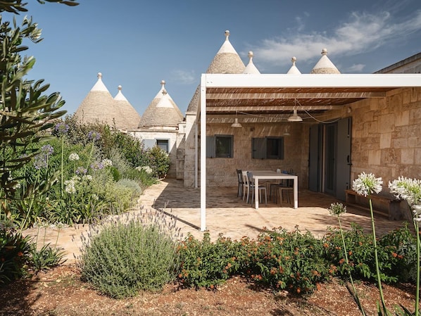 A courtyard with a stone building, a covered seating area, and a garden with various plants. - Trulli near Fontanella, with a pool (Martina Franca)